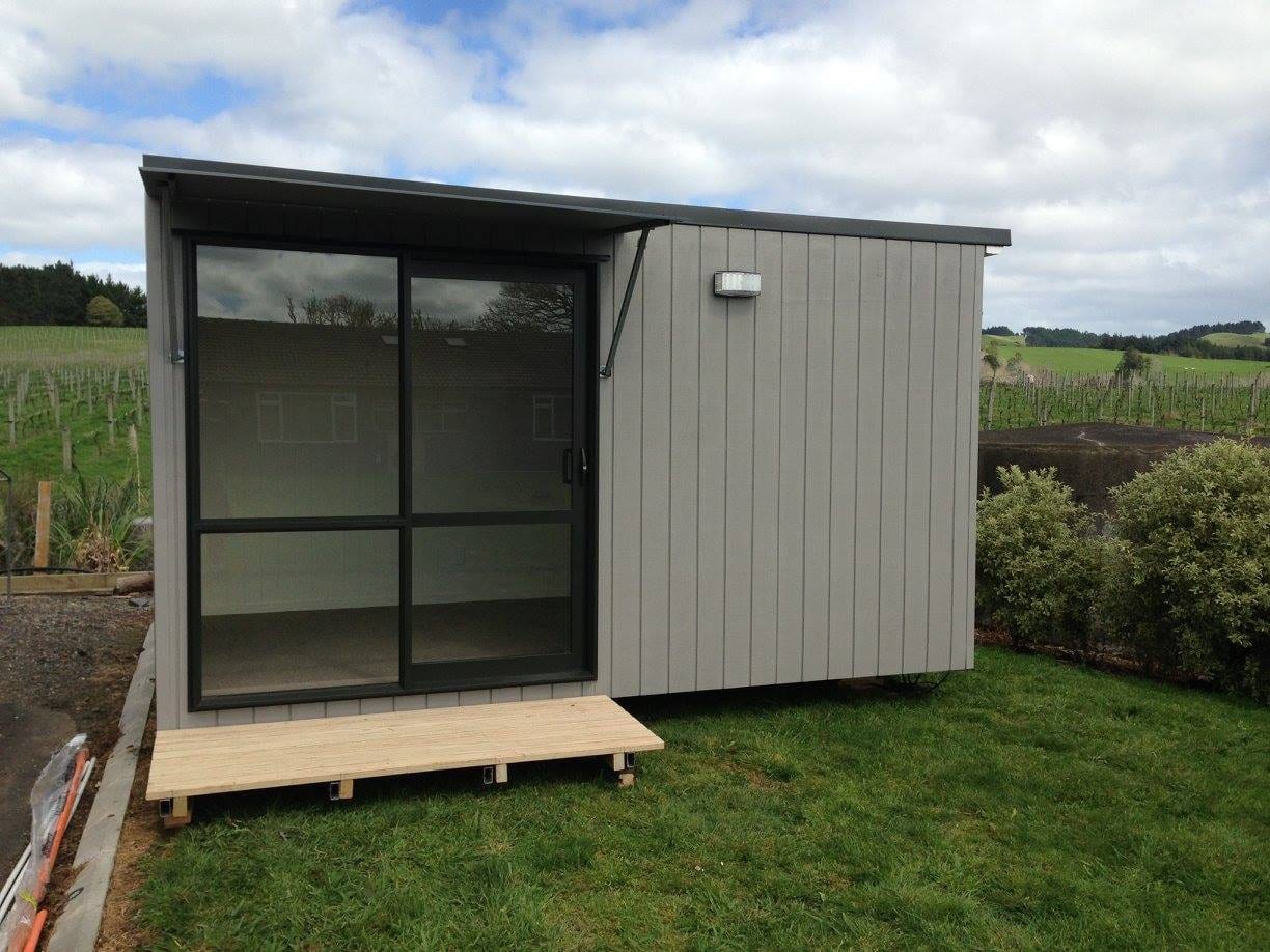 A Moreroom portable cabin with a sliding glass door and timber deck, set in a New Zealand vineyard